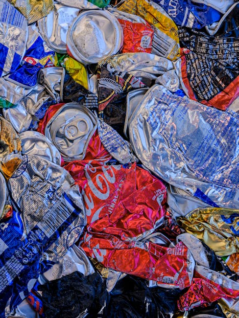 Close-up image of a pile of crushed aluminum cans and plastic bottles, primarily from beverages such as Coca-Cola, with visible brand logos and colorful packaging. The cans and bottles are metallic and plastic, showing signs of being discarded and crumpled. The background is indiscernible, emphasizing the tangled, compacted waste materials. The scene reflects waste collection and recycling efforts relevant to rubbish disposal rules in Westminster, illustrating the importance of proper waste separation and environmental hygiene. Cleaners W9 specializes in surface cleaning and waste management services, supporting compliance with local council regulations for rubbish disposal in Maida Vale, W9.